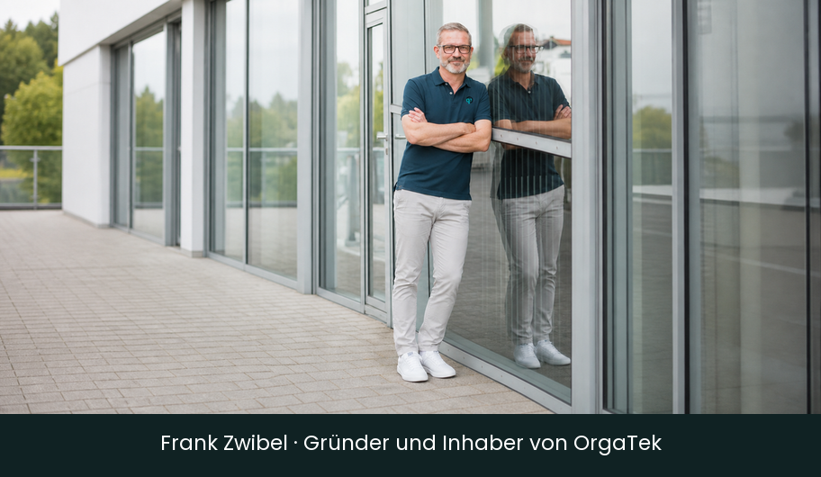 Frank Zwibel vor einer industriellen Glasfassade mit sichtbarer Spiegelung.